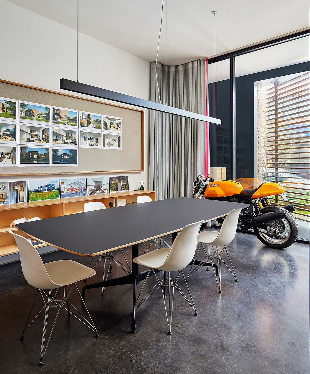 Modern open-concept room with sleek black table, white chairs, and motorcycle display.