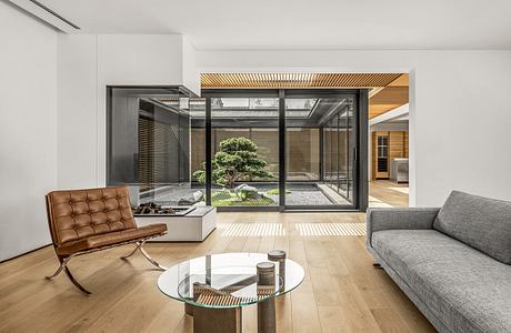 Elegant modern living space with glass walls, wooden accents, and a serene indoor garden.