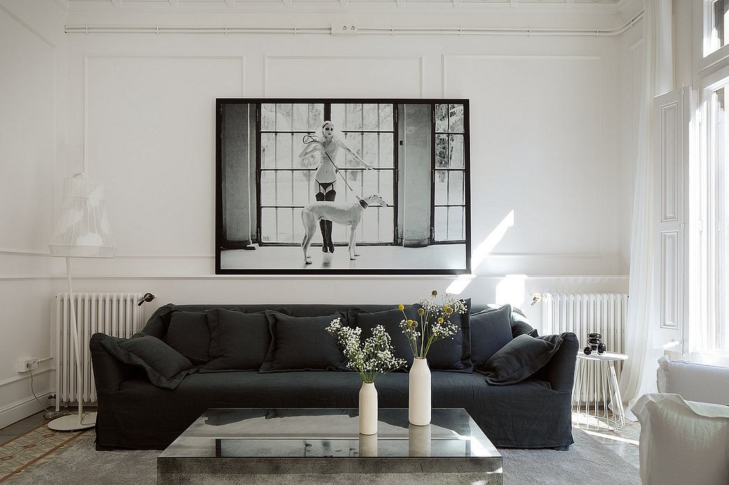 Spacious, minimalist living room with large framed artwork, black sofa, and glass coffee table.