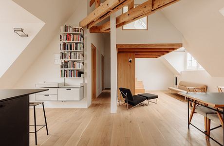 Airy loft space with exposed wooden beams, built-in bookshelf, and minimalist furnishings.