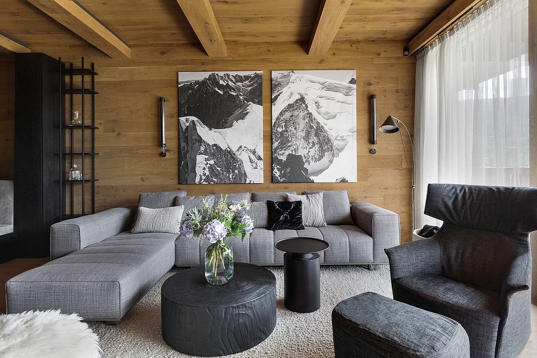 Rustic chalet interior with wood beams, gray sofas, and large black-and-white landscape art.