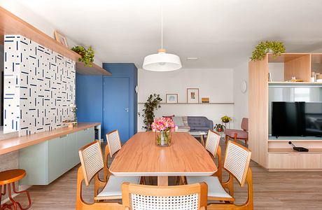 A modern, open-concept living space with a wood dining table, built-in shelves, and a patterned accent wall.