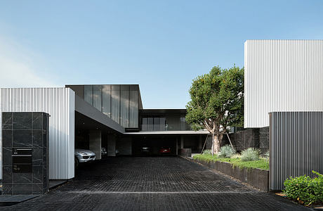 Modern building with sleek lines, glass panels, and a large tree in the foreground.