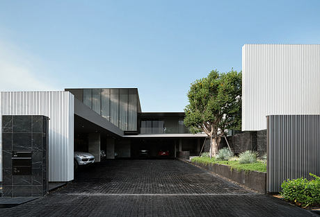 Modern building with sleek lines, glass panels, and a large tree in the foreground.