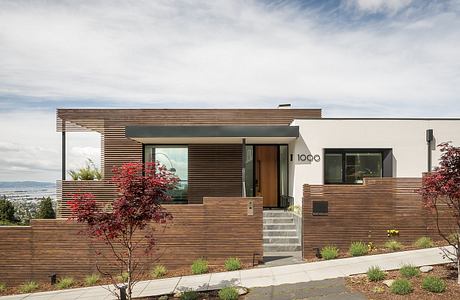 Modern wood-paneled home with expansive windows, landscaped yard, and architectural details.