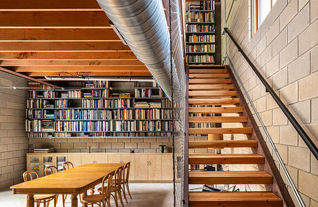 Rustic industrial interior with wooden staircase, bookshelves, and dining table.