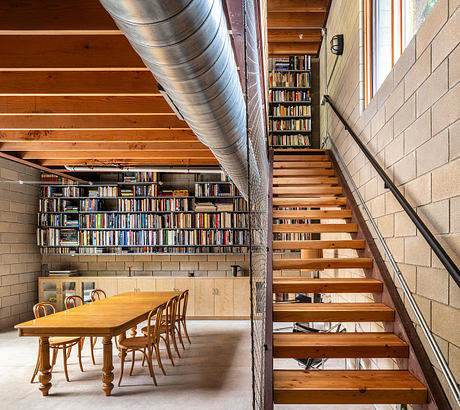 Rustic industrial interior with wooden staircase, bookshelves, and dining table.