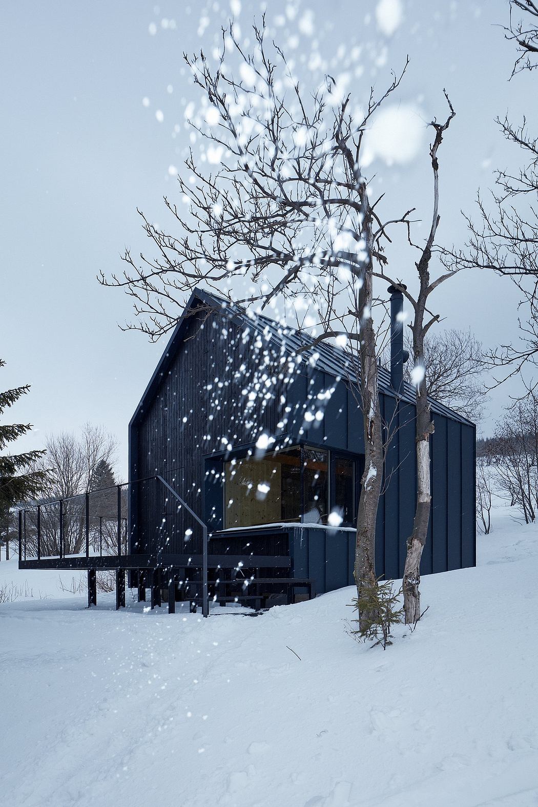A modern, black cabin nestled in a snowy landscape, with bare trees and snowfall creating a peaceful scene.