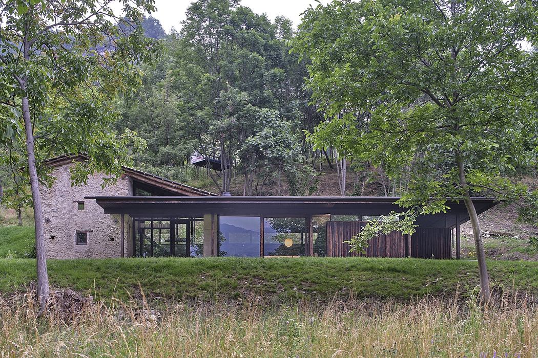 A modern, glass-walled cabin nestled in a lush forest, offering views of the surrounding landscape.
