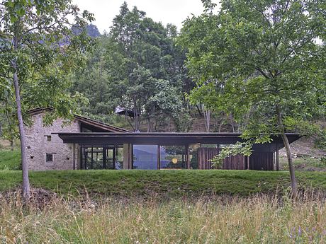 A modern, glass-walled cabin nestled in a lush forest, offering views of the surrounding landscape.