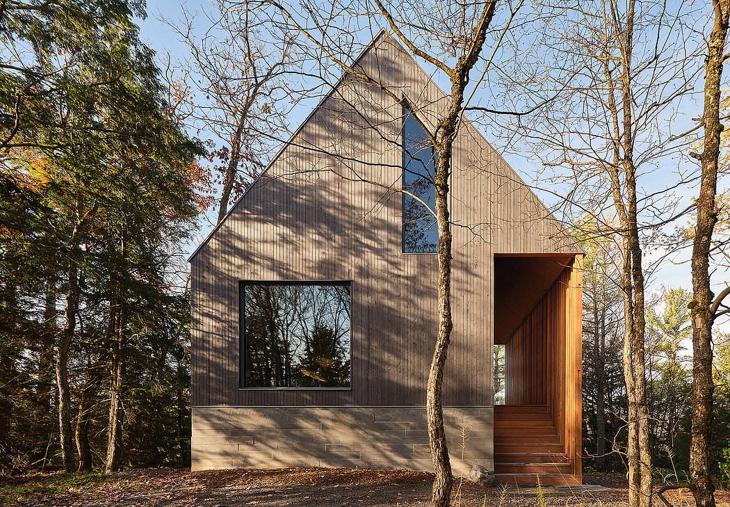 A modern, minimalist cabin nestled among trees, with clean lines, large windows, and a warm wood entrance.