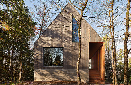 A modern, minimalist cabin nestled among trees, with clean lines, large windows, and a warm wood entrance.