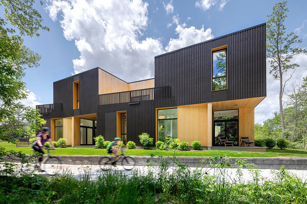 A modern, modular home with a mix of black siding and wood accents, surrounded by lush greenery.