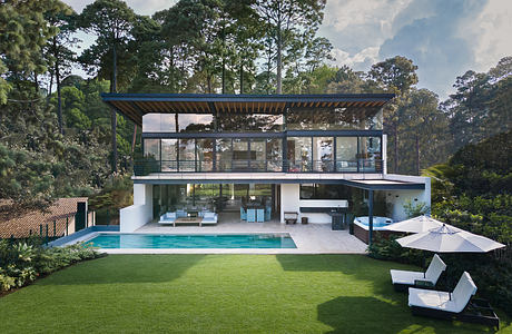 A modern glass-walled home with a swimming pool, surrounded by lush greenery.