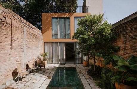 A modern, glass-walled building surrounded by lush greenery and a small reflecting pool.