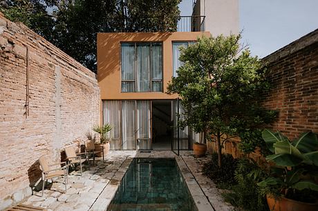 A modern, glass-walled building surrounded by lush greenery and a small reflecting pool.