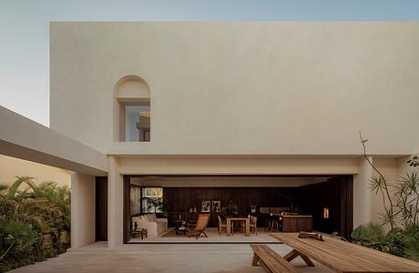 Minimalist contemporary architecture with arched entryway, wooden furnishings, and lush greenery.