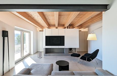 Minimalist living room with exposed wooden beams, built-in storage, and large windows.