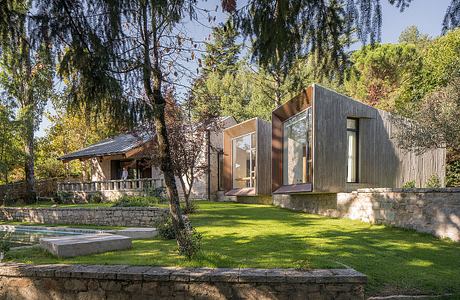 Modern wooden and glass home set in lush, wooded landscape with pool and stone patio.