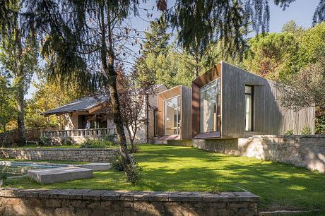 Modern wooden and glass home set in lush, wooded landscape with pool and stone patio.