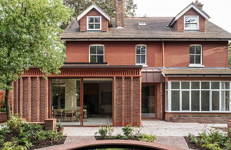 A two-story brick home with dormers, an extended porch, and large windows overlooking a landscaped garden.