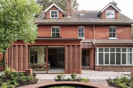 A two-story brick home with dormers, an extended porch, and large windows overlooking a landscaped garden.