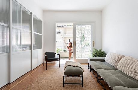 Minimal, open-concept living space with sliding glass panels, plush seating, and plant decor.