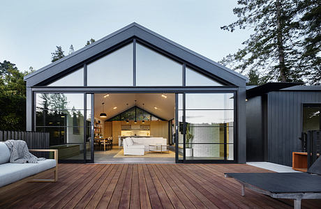 Contemporary glass-walled home with open-concept living space, wood deck, and modern furnishings.