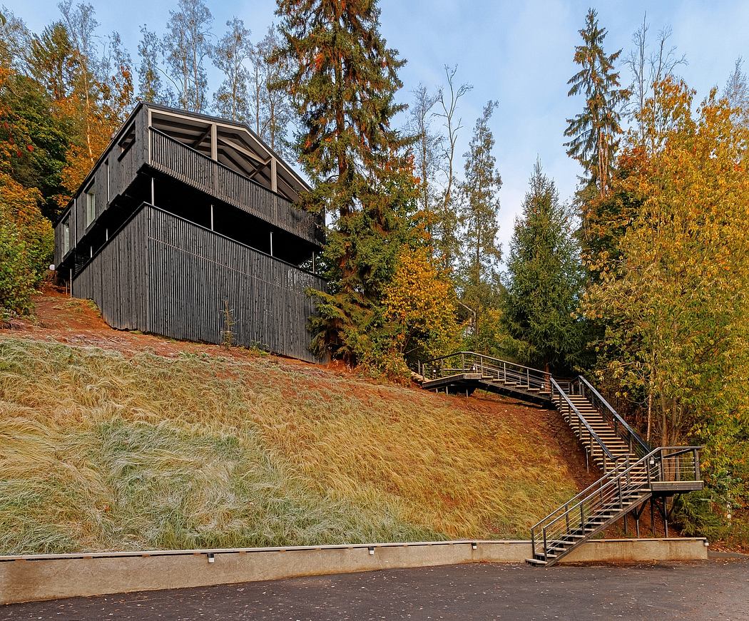 A multi-level wooden structure nestled in an autumn forest, with stairs leading to the entrance.