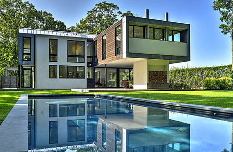 A modern, two-story home with clean lines, large windows, and a reflection pool in the foreground.