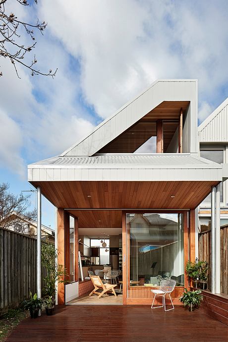 Sleek modern design featuring angled roof, wood paneling, and large glass doors opening to patio.