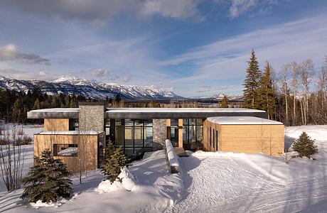 A modern, geometric mountain home with wood and stone accents, surrounded by snowy landscape.