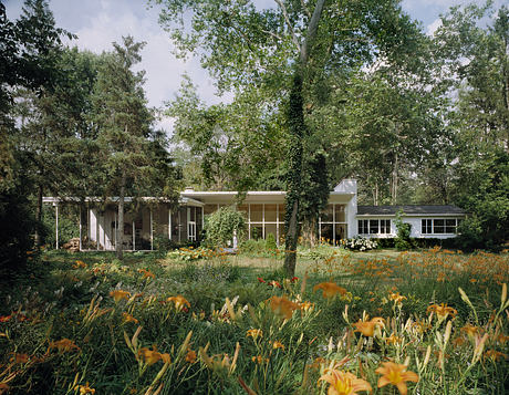 A mid-century modern home surrounded by lush greenery and vibrant flowers.