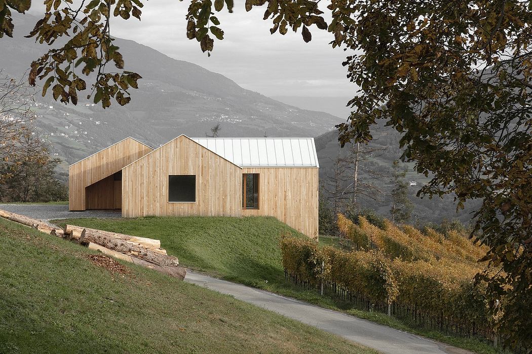 A modern wooden barn-style structure nestled in a lush, mountainous landscape.
