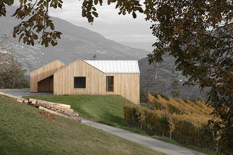 A modern wooden barn-style structure nestled in a lush, mountainous landscape.