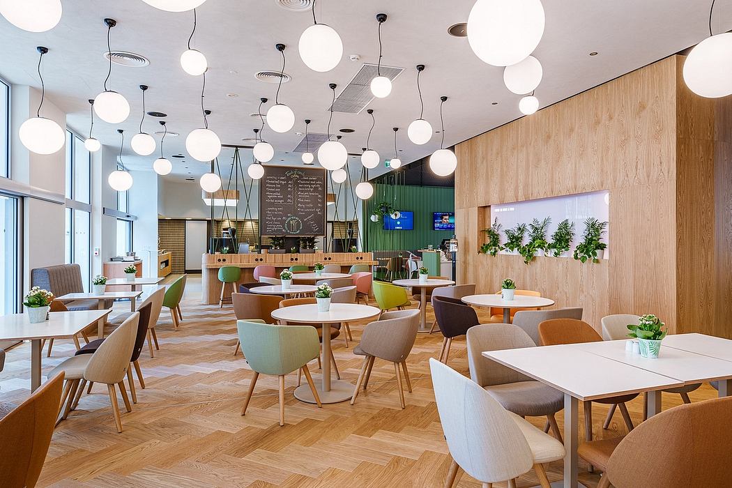 Modern, open-plan cafe interior with wooden walls, hanging globe lights, and colorful chairs.