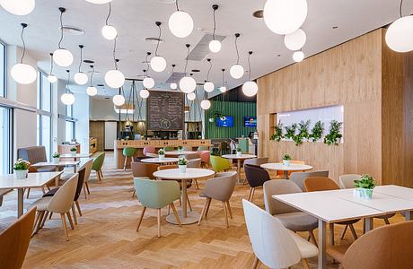 Modern, open-plan cafe interior with wooden walls, hanging globe lights, and colorful chairs.