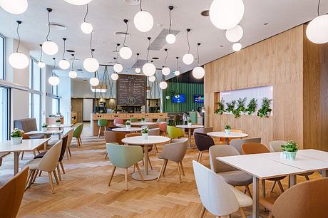 Modern, open-plan cafe interior with wooden walls, hanging globe lights, and colorful chairs.