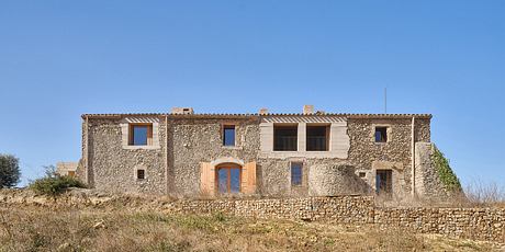 Rustic stone farmhouse with arched windows, carved wooden doors, and tiered roofs.