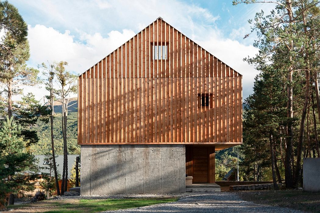 A modern wooden cabin structure with a steep gable roof and concrete foundation, set amid pine trees.
