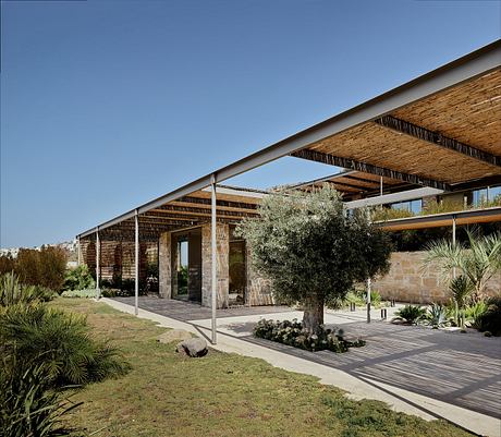 A modern architectural structure with bamboo and glass elements, surrounded by lush vegetation.