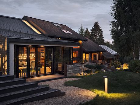 A modern rustic house with expansive windows, a covered patio, and well-lit interiors.