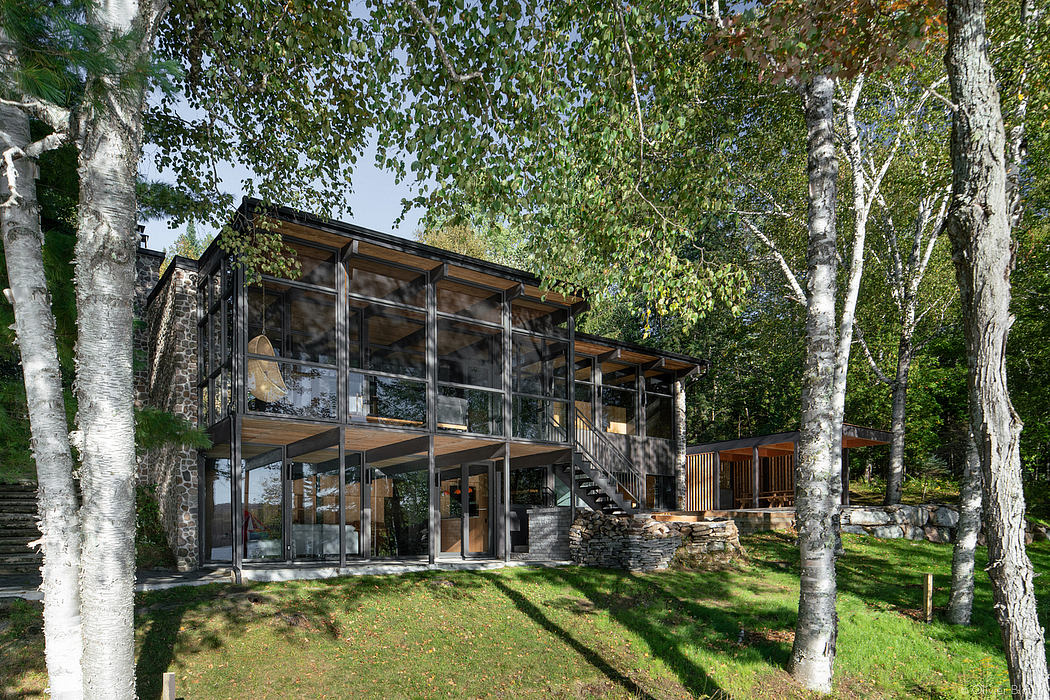 Striking modern glass and wood cabin nestled in lush forest, with sleek architectural design.