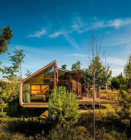 A wooden cabin with a large triangular window nestled in a lush, verdant landscape.