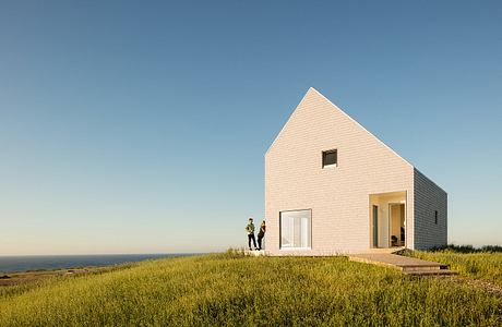 A modern, minimalist house with a striking triangular roof and large windows overlooking the landscape.