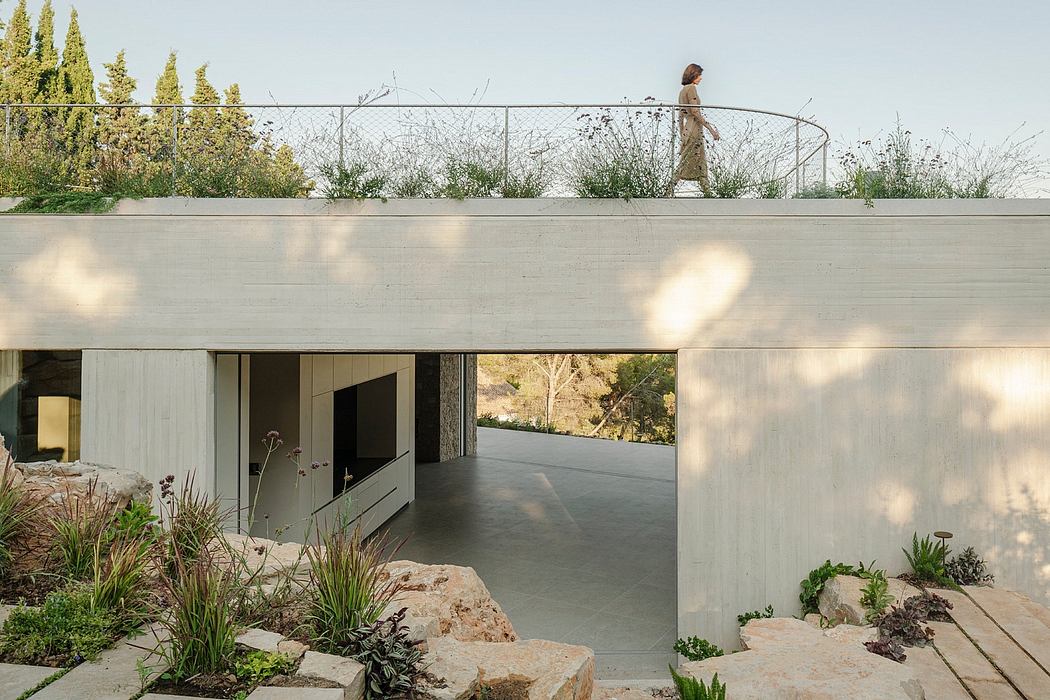Modern concrete structure with clean lines, greenery, and a person on the rooftop.