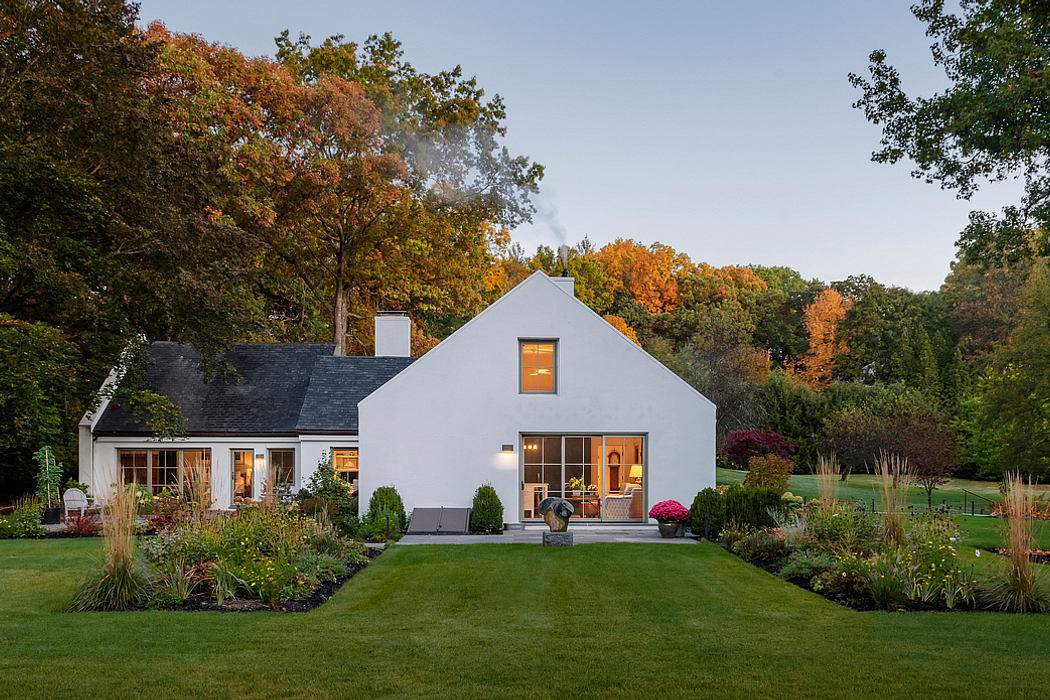 Beautiful autumn-colored trees frame a quaint, modern farmhouse with warm interior lighting.