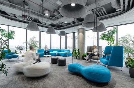 Modern office lounge with minimalist decor, vibrant blue furniture, and lush greenery.