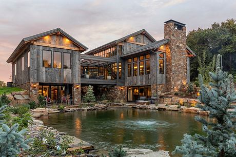 A rustic mountain cabin with stone chimney, wooden siding, and a tranquil pond.