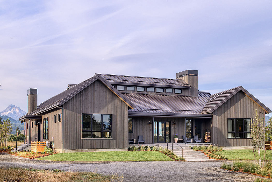 Rustic modern home with gabled roof, large windows, and wooden siding against mountain backdrop.